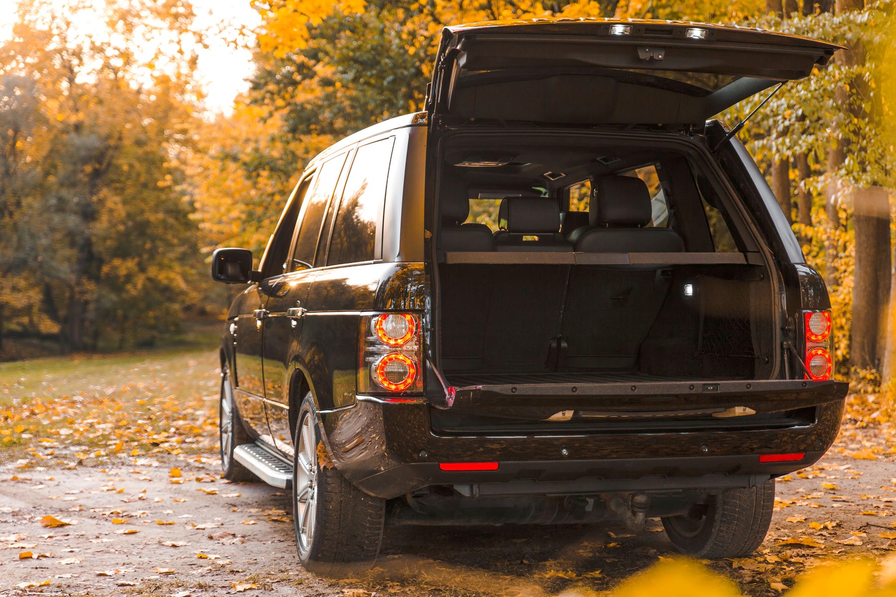 A Range Rover with the boot open on a wooded autumn track.